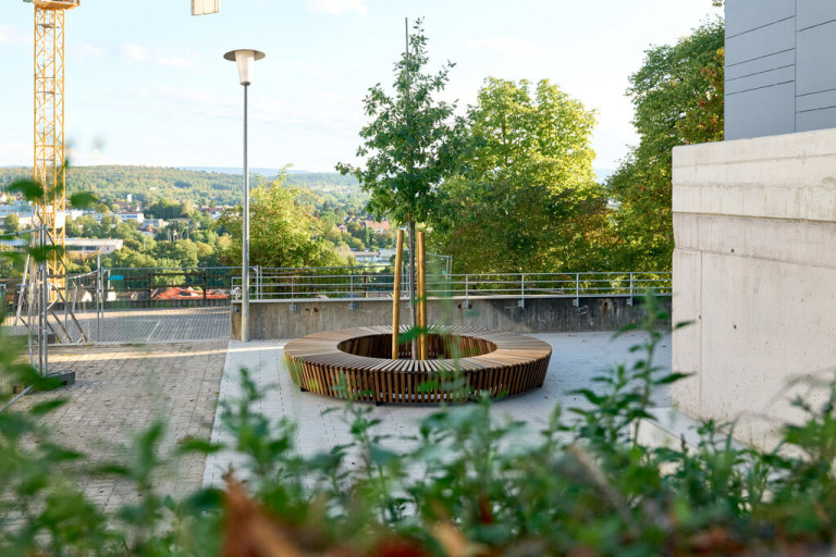 Runde Sitzbank aus Holz um einen Baum auf dem Gelände von Grüner Daumen in Remchingen, modernes Stadtmobiliar im Freien