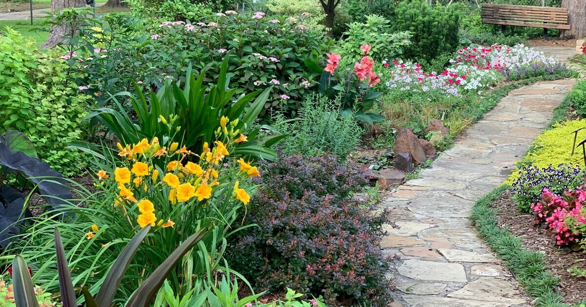 Gartenweg mit bunten Blumen und Natursteinplatten im Sommer