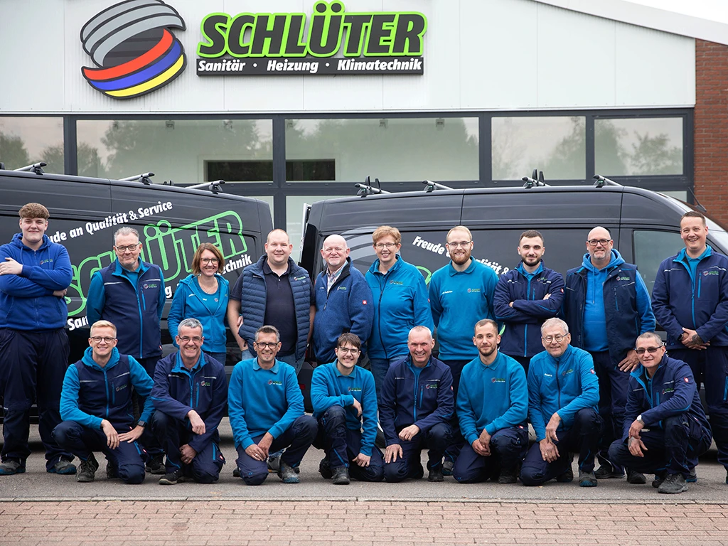 Teamfoto der Firma Schlüter Sanitär, Heizung und Klimatechnik vor dem Firmengebäude und den Firmenfahrzeugen