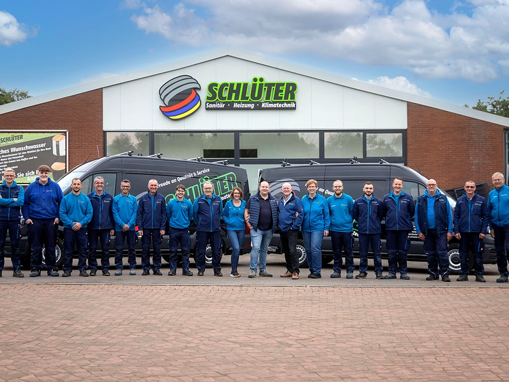Teamfoto der Firma Schlüter Sanitär, Heizung, Klimatechnik vor dem Firmengebäude und Firmenfahrzeugen