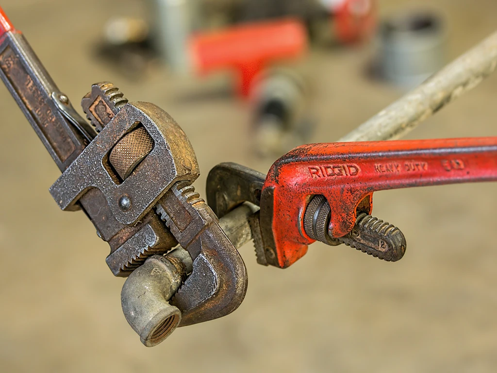 Zwei Rohrzangen, darunter eine rote RIDGID Heavy Duty Rohrzange, greifen ein Metallrohr – Werkzeug für Installateure und Handwerker.