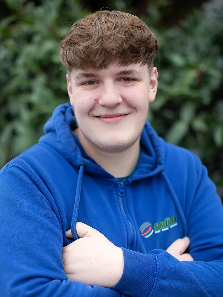Mats Hoke im blauen Schlüter Arbeitskleidung Pullover vor grüner Naturkulisse