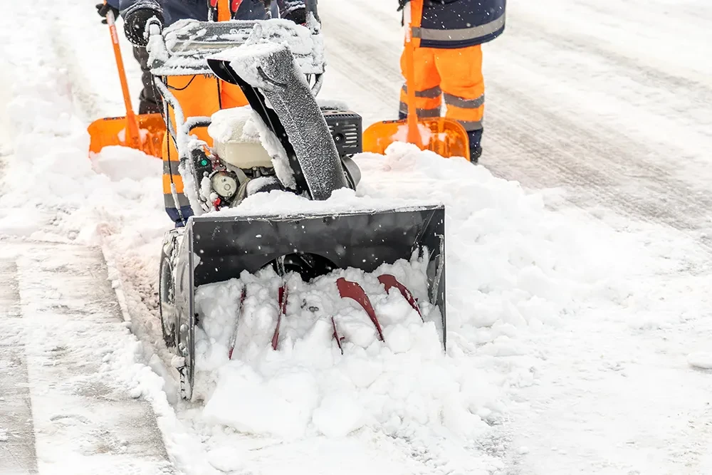Winterdienst beim Schneeräumen mit Schneefräse und Schneeschaufel auf verschneiter Straße