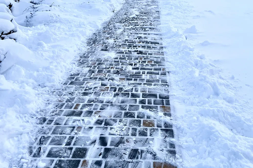 Gepflasterter Weg im Winter mit Schnee an den Seiten, teilweise freigeräumt