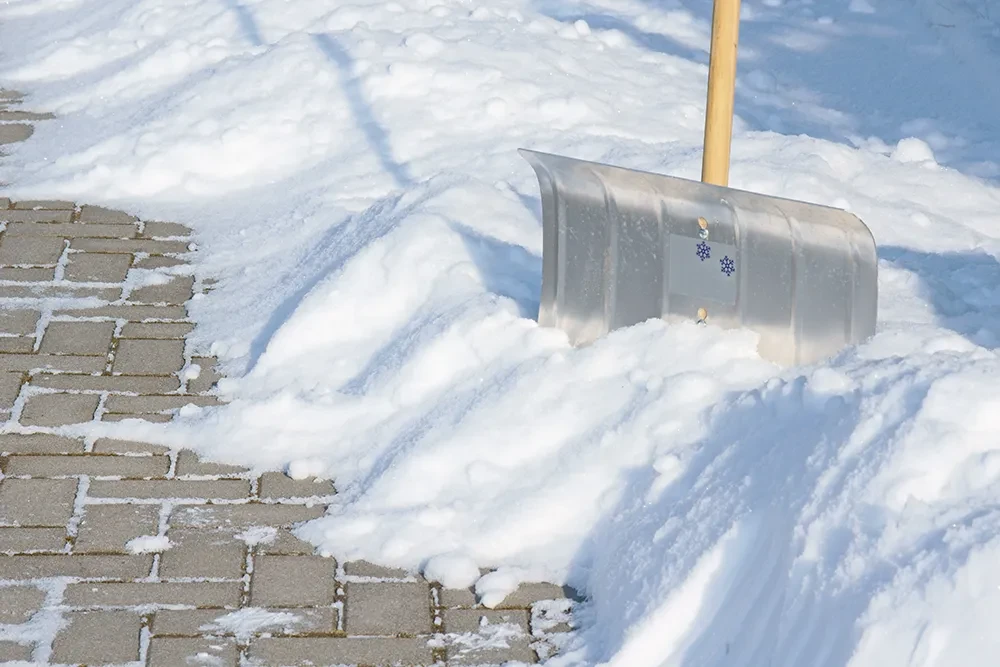 Schneeschaufel beim Schneeräumen auf einem gepflasterten Gehweg im Winter