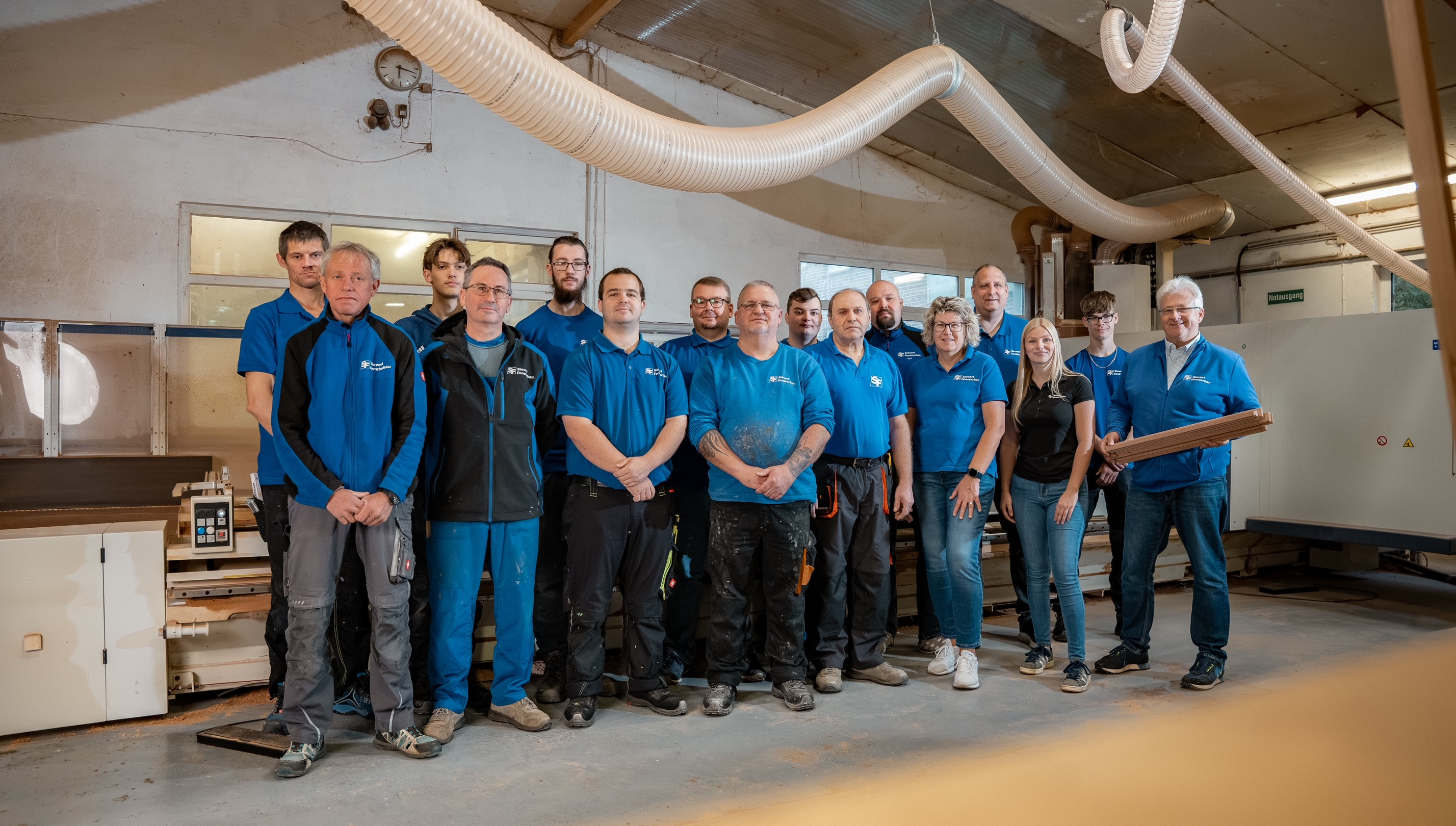 Gruppenfoto eines Handwerkerteams in einer Werkstatt, alle tragen blaue Arbeitskleidung