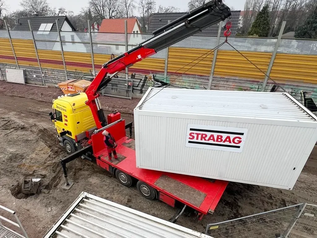 Denis Schenk Logistik transportiert STRABAG Container per LKW-Kran auf Baustelle Denis Schenk Logistik LKW mit Kran hebt STRABAG Container auf Baustelle