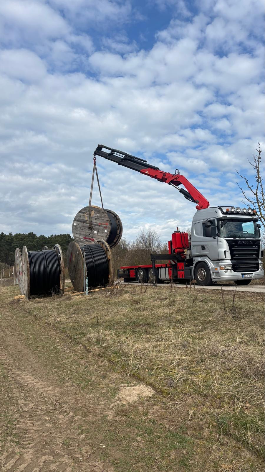 Scania LKW mit Ladekran hebt Kabeltrommel auf einer Baustelle im Freien