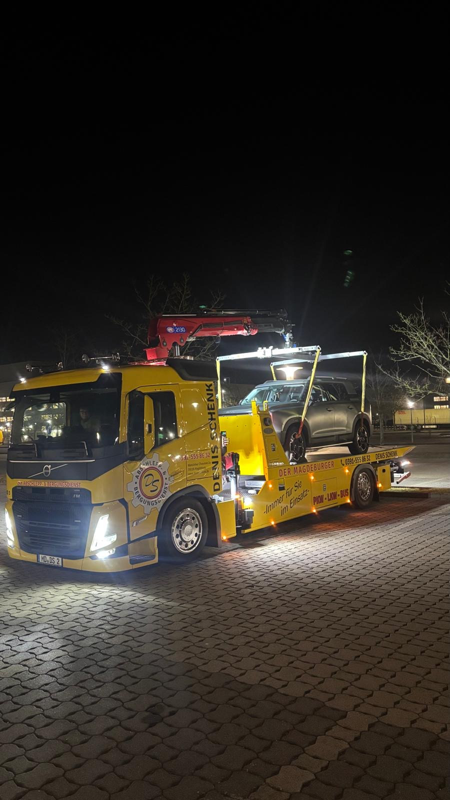 Volvo Abschleppwagen transportiert Auto nachts auf Parkplatz