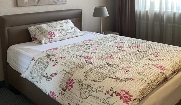 Zimmer Start – gemütliches Schlafzimmer mit floralem Bettbezug und Nachttischlampe