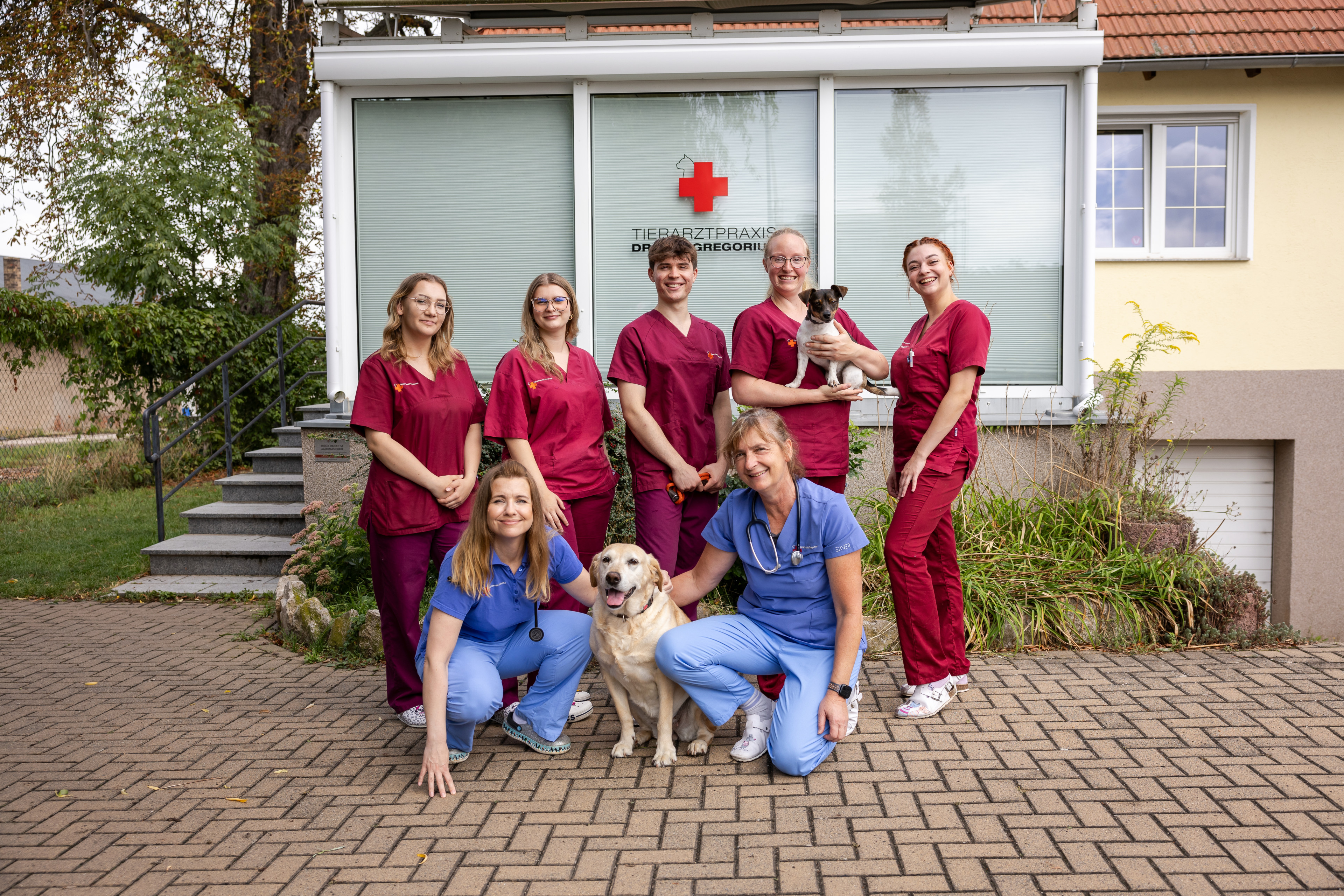 Team der Tierarztpraxis Dr. Gregor in Arbeitskleidung mit Hunden vor der Praxis