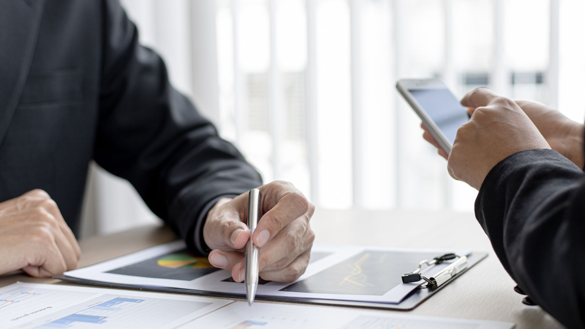 Vorteile barrierefreie Website für Unternehmen Hand hält Stift und deutet auf eine Grafik, während eine andere Hand auf ein Smartphone tippt