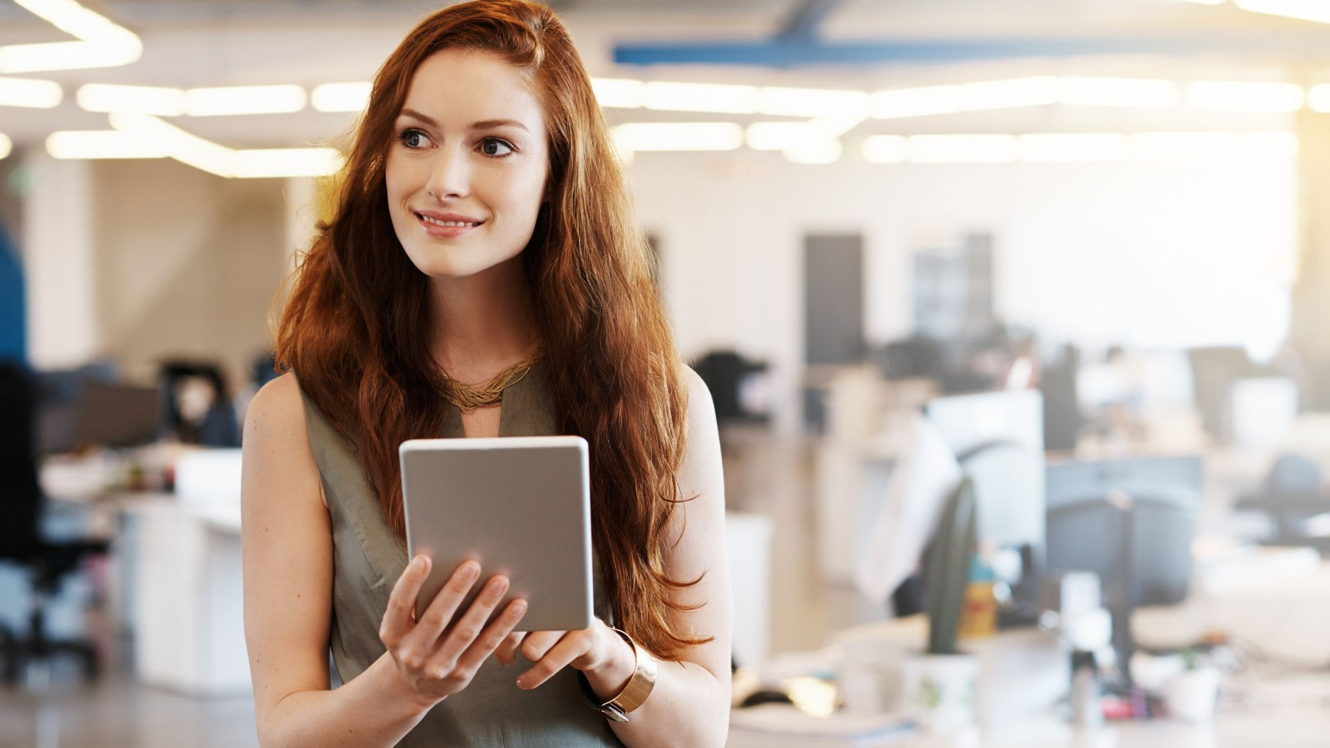 Frau mit langen roten Haaren hält ein Tablet im modernen Büro