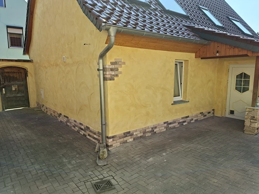 Fassadenreferenz von CW Partnerputz mit gelbem Putz und Klinkerstein-Details am Sockel