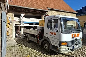 Leistungen Mauerarbeiten – Bauarbeiter bei Mauerarbeiten an einem Gebäude mit LKW vor Ort