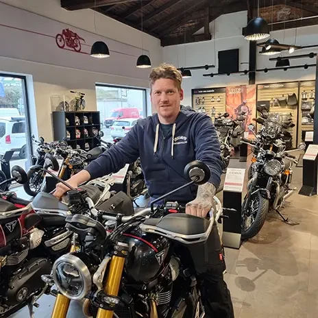 Mario Wilking auf einem Motorrad im Motorradgeschäft umgeben von Triumph Motorrädern