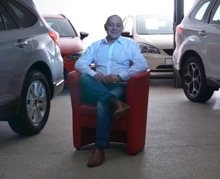 Heiko Lübkemann sitzt auf einem roten Sessel zwischen Autos im Autohaus