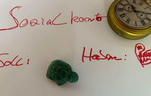 sozialkonto: Handschrift und Schildkröte mit Uhr auf Papier Handschriftlicher Schriftzug 'sozialkonto' und 'Hasan' auf Papier mit grüner Schildkrötenfigur und Uhr