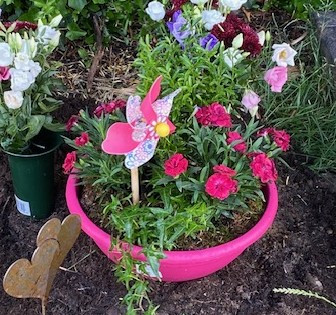 Was treibt mich an im Leben – Blumen im Garten mit Windrad in pinkem Topf Blumenarrangement im Garten mit pinkem Blumentopf und Windrad – was treibt mich an im Leben