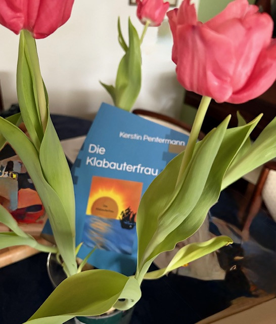 Buch Die Klabauterfrau von Kerstin Pentermann hinter rosa Tulpen, Nahaufnahme