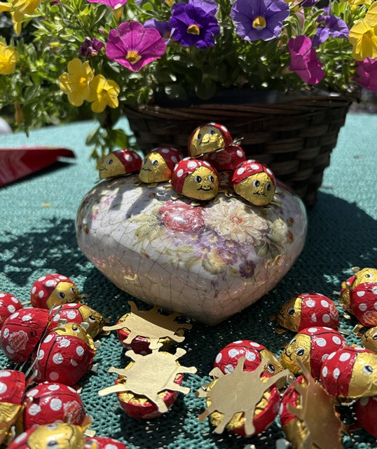 Schokoladen-Käfer auf einer Porzellandose mit Blumenmuster und bunten Blüten im Hintergrund