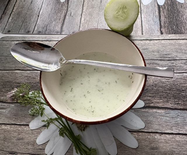 Gurkensuppe in einer Schüssel mit Löffel und frischer Gurke auf Holztisch