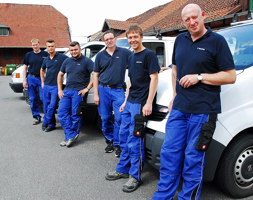 Das Borchers Team in blauer Arbeitskleidung vor Firmenfahrzeugen