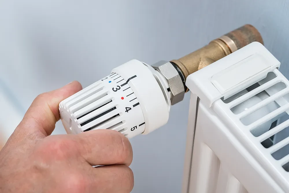 Hand am Thermostat eines Heizkörpers zur Temperaturregelung