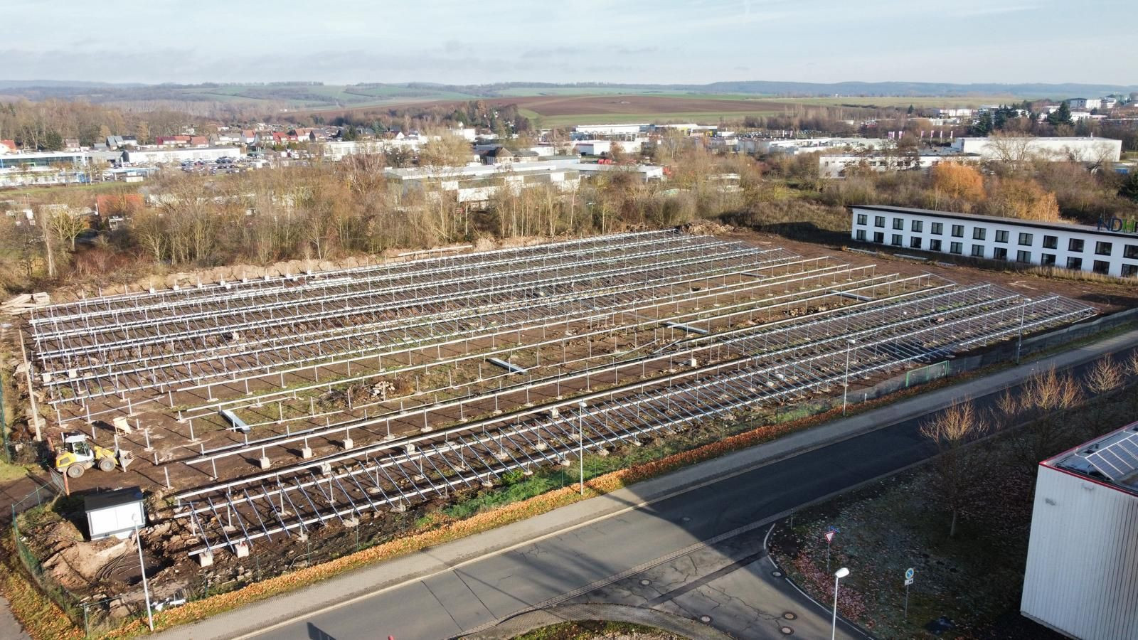 Bau einer Photovoltaikanlage auf einem Feld am Stadtrand, Metallgestelle für Solarmodule, Industriegebiet im Hintergrund