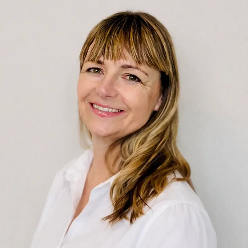 Porträtfoto von Antje in weißer Bluse vor hellem Hintergrund