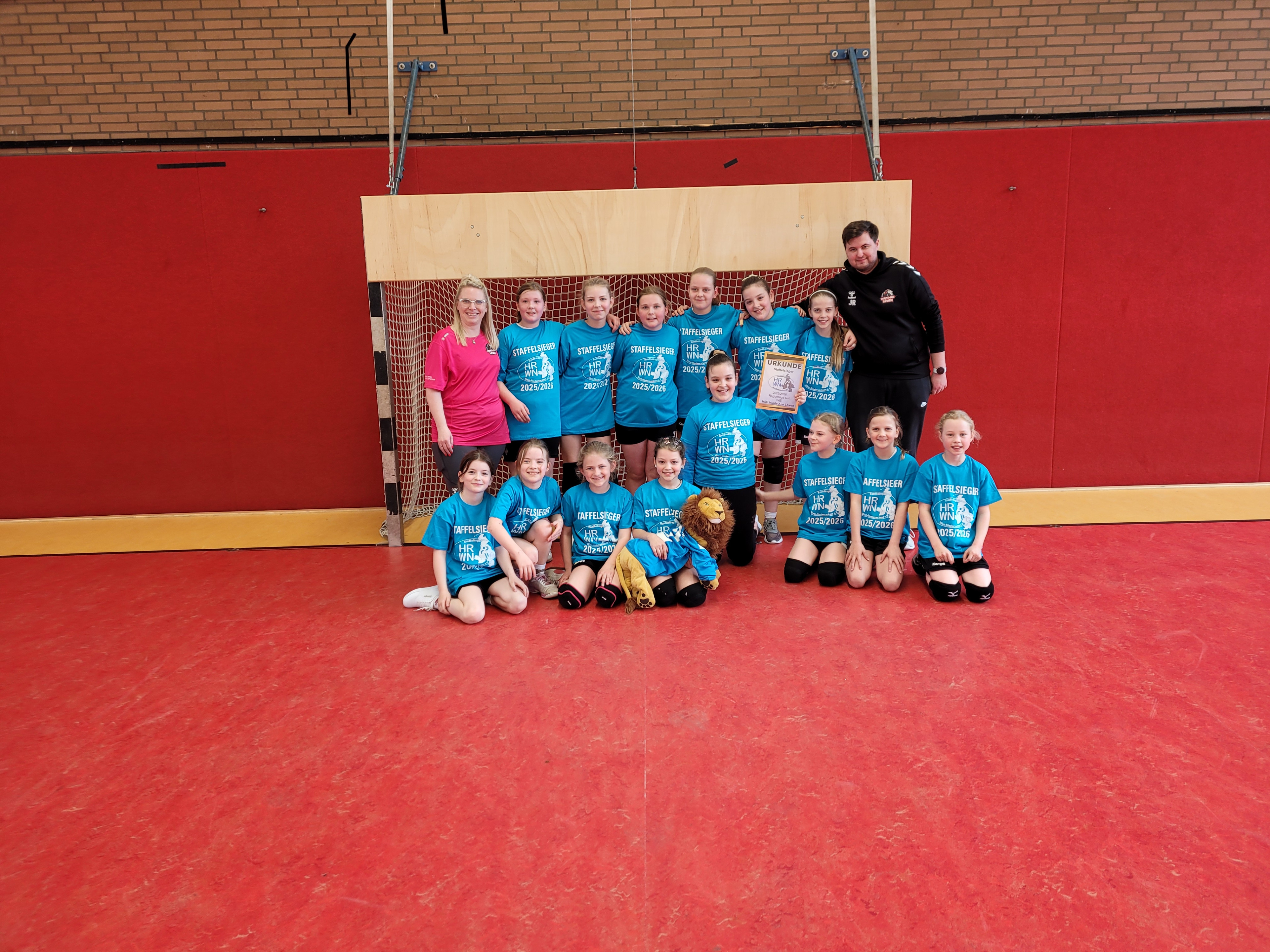 Gruppenfoto der Huntel Aue Löwen WJE Handballmannschaft mit Trainerteam in der Sporthalle, Staffelmeister 2023/2024