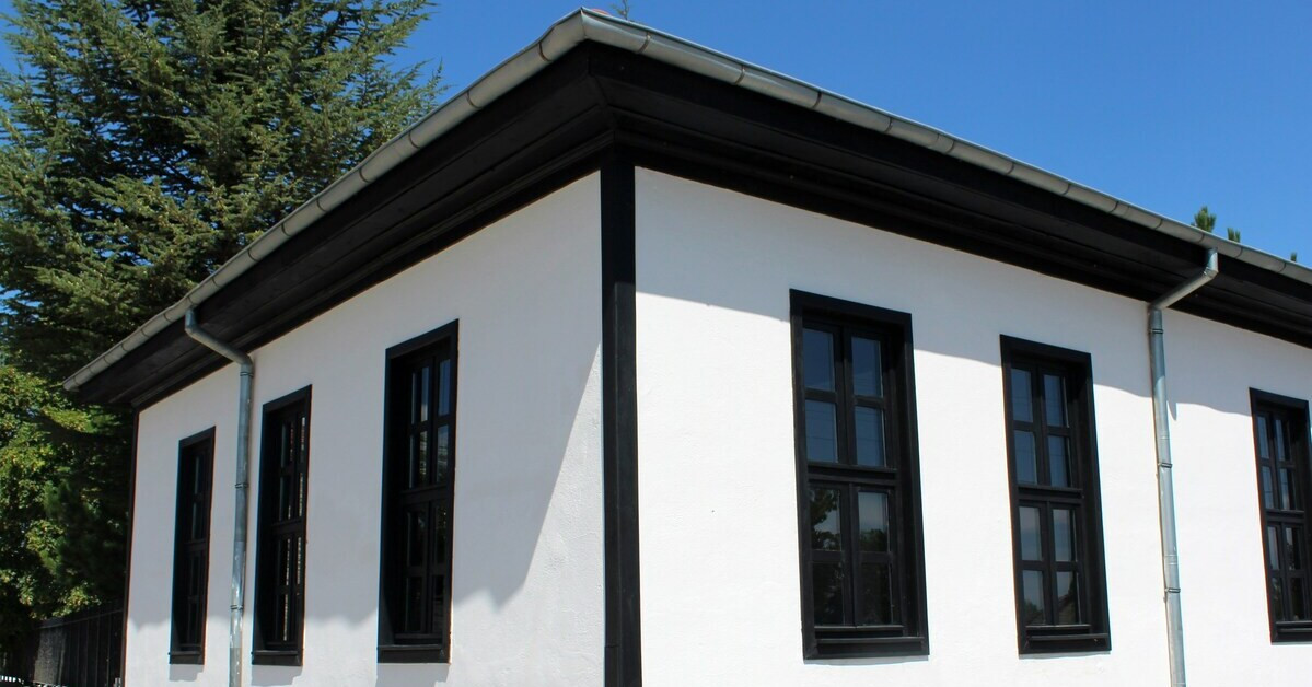 Weiße Hauswand mit schwarzen Fensterrahmen und Dachrinne Weiße Hauswand mit schwarzen Fensterrahmen und Dachrinne bei sonnigem Wetter