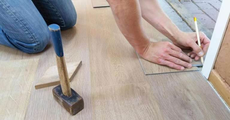 Boden verlegen: Laminatboden fachgerecht verlegen mit Werkzeugen Boden verlegen – Handwerker verlegt Laminatboden mit Hammer und Holzstück
