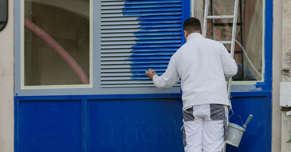 Handwerker beim Fassade streichen mit blauer Farbe