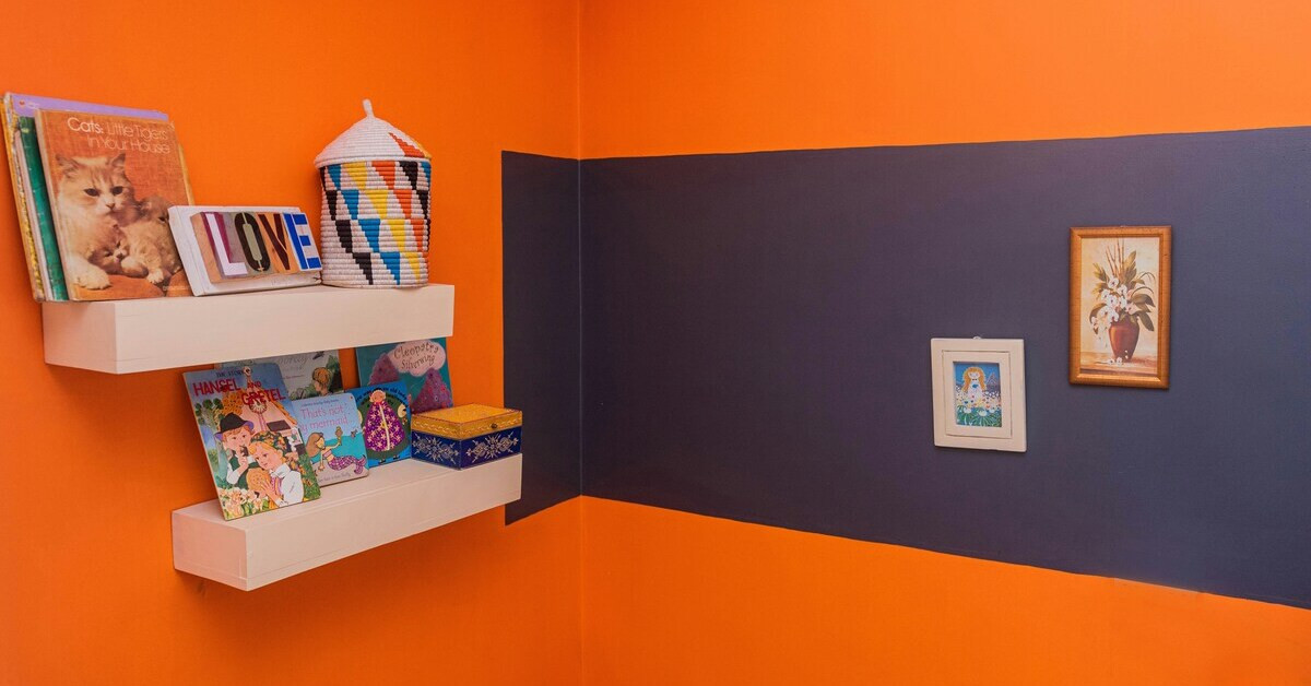 Bunte Wandgestaltung im Kinderzimmer mit orangefarbenem und dunkelblauem Anstrich sowie Regal mit Kinderbüchern und Dekoration