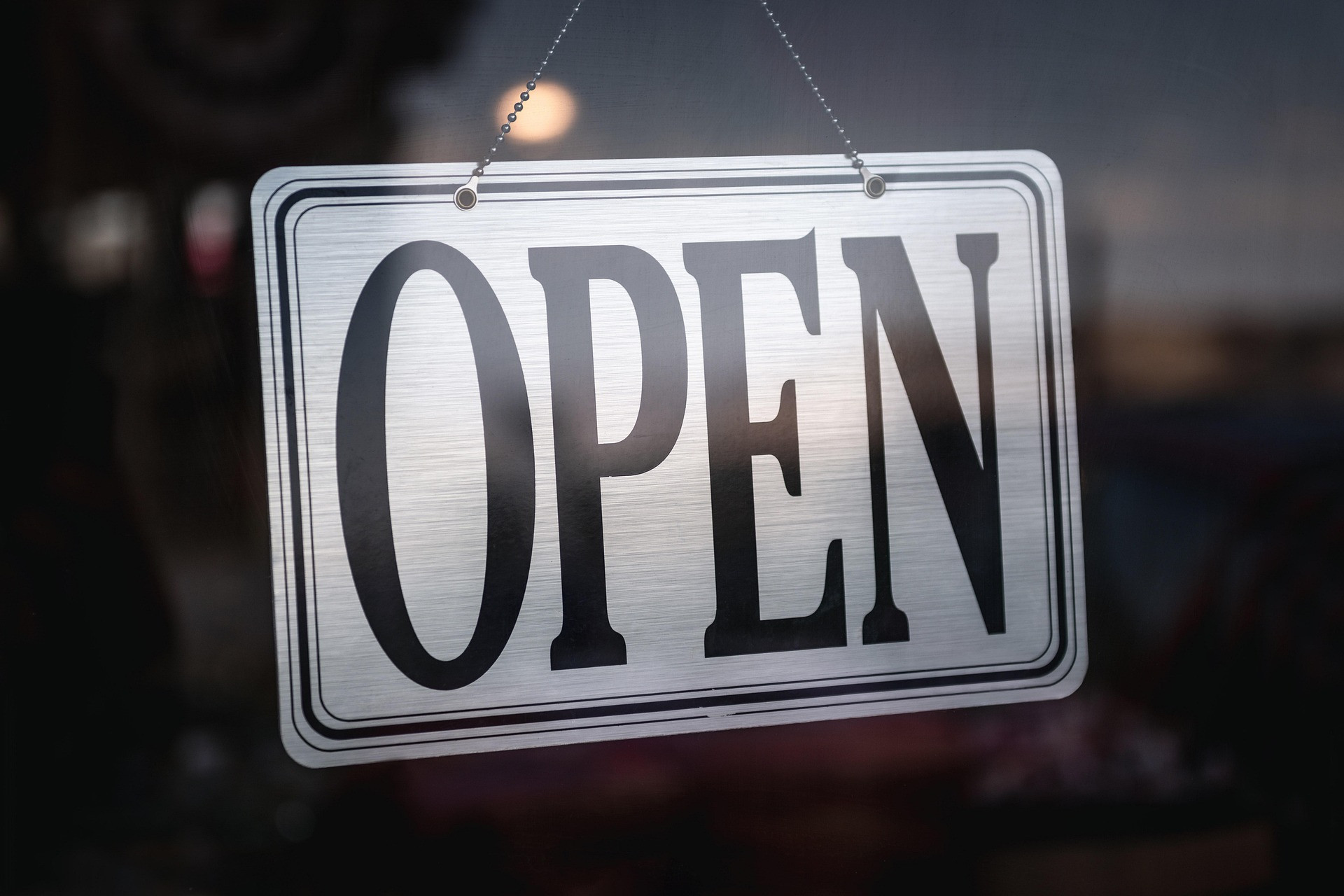 Metallschild mit der Aufschrift 'OPEN' vor einem Ladenfenster