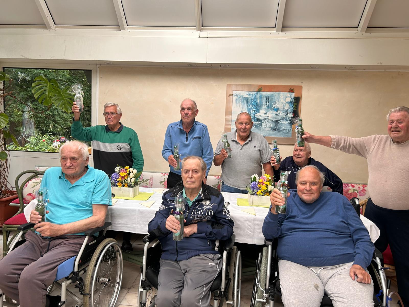 Seniorengruppe bei einer Feier mit Blumen und Getränken im Mai 2025