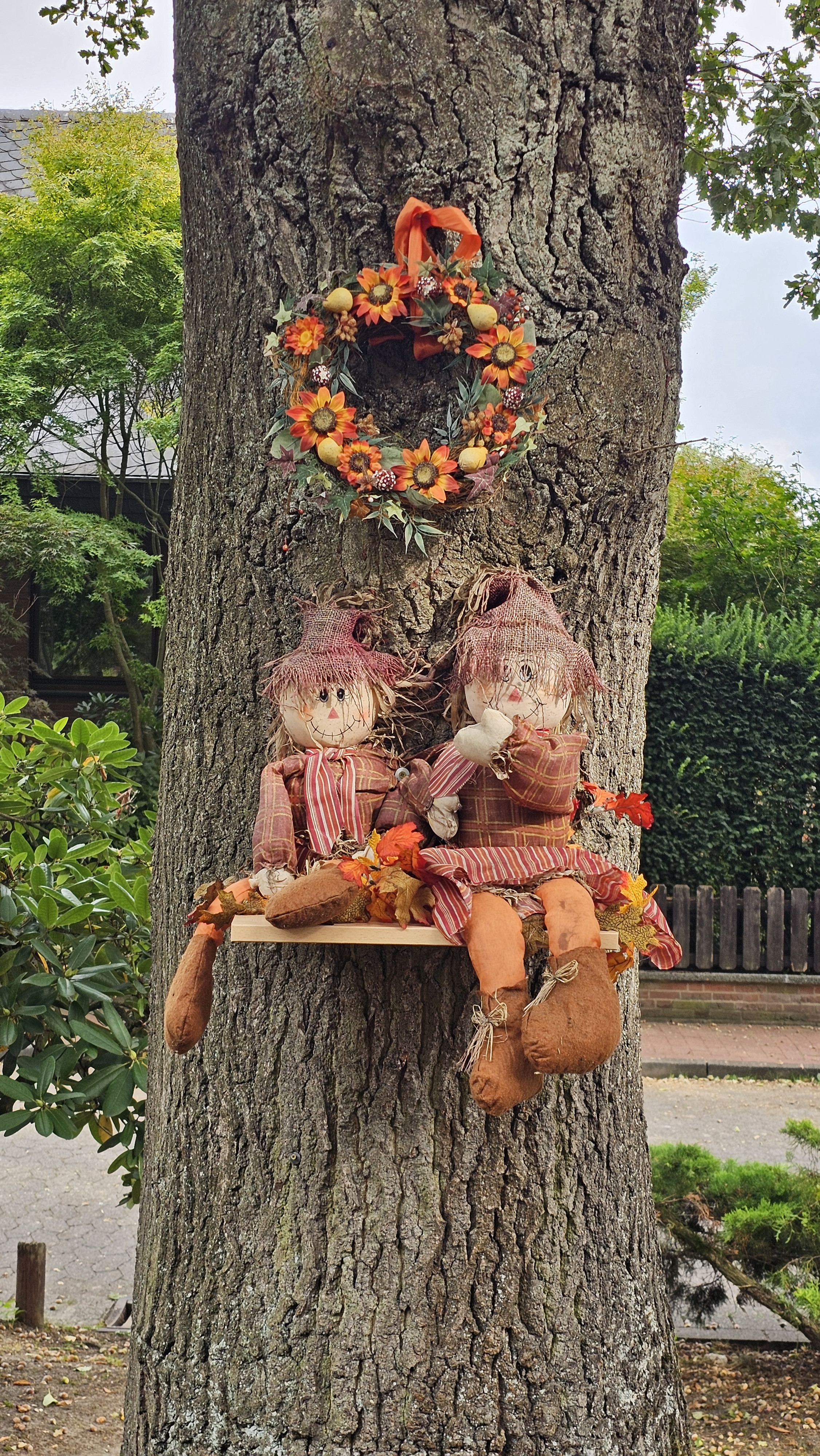 Herbstliche Vogelscheuchen-Dekoration an einem Baum mit Blumenkranz