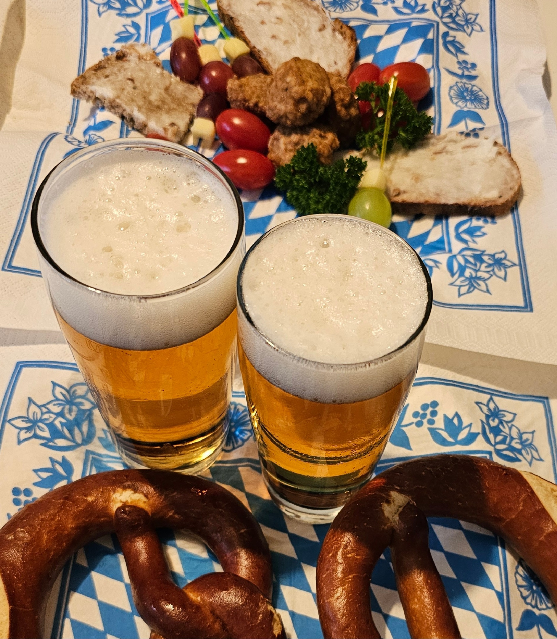 Zwei Gläser Bier, Brezeln und bayerische Spezialitäten auf einem Tisch beim Oktoberfest