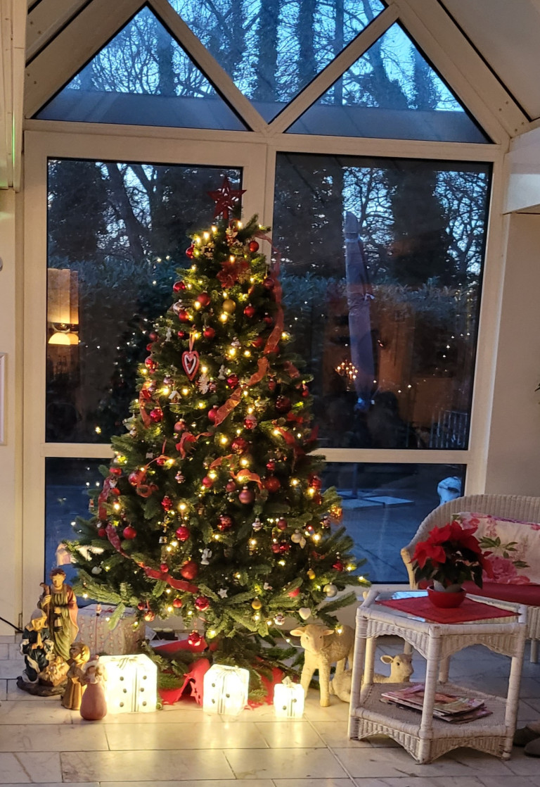 Weihnachtsbaum mit roten und goldenen Kugeln und Lichterketten in einem Wohnzimmer am Abend
