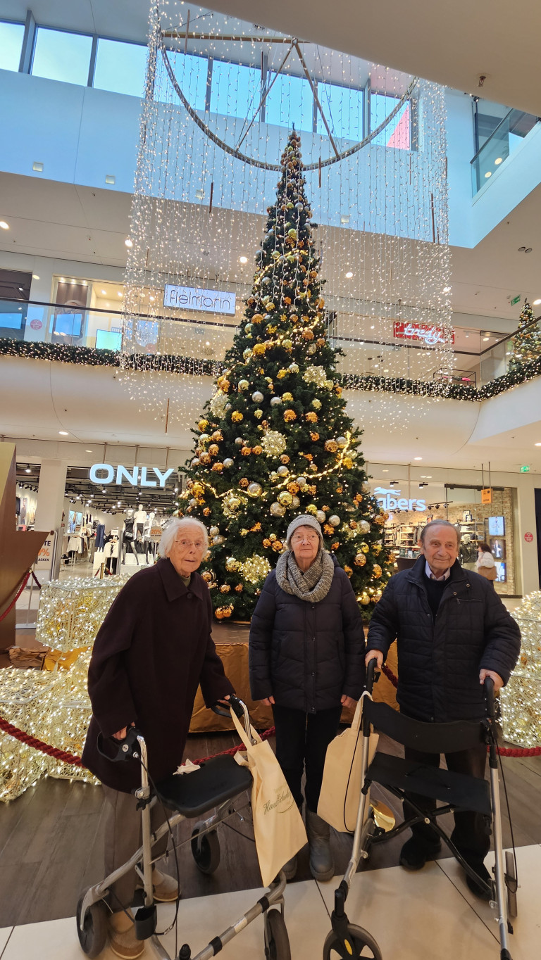 Weihnachtsbaum und festliche Dekoration im Einkaufszentrum mit älteren Menschen im Vordergrund