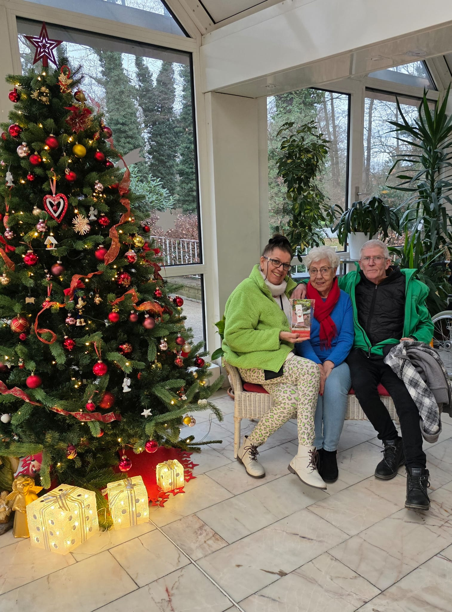 Weihnachtsbaum und drei Personen auf einer Bank im Wintergarten mit Geschenken