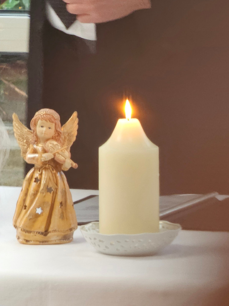 Kerze und Engel als Weihnachtsdekoration am 21. Dezember 2025 Kerze und goldener Engel mit Geige auf Tisch, festliche Dekoration am 21.12.2025