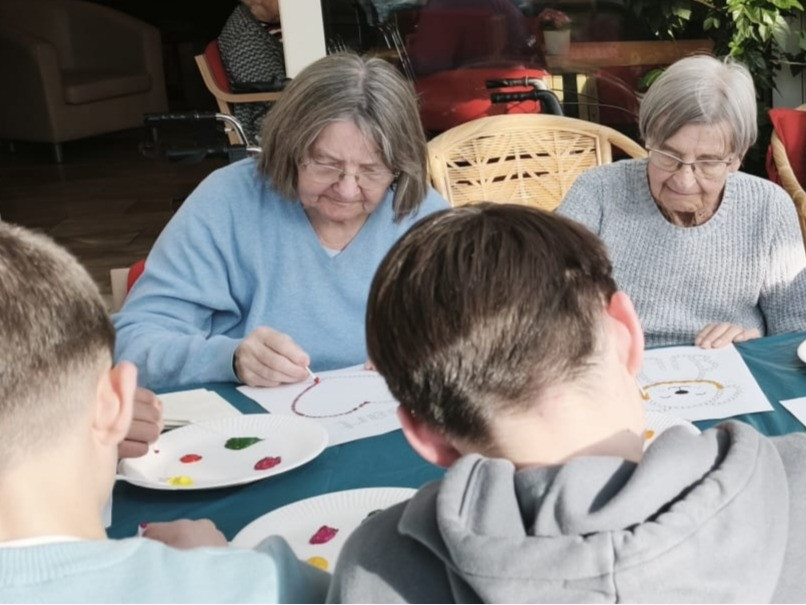 Senioren und Kinder beim gemeinsamen Malen an einem Tisch im Seniorenheim