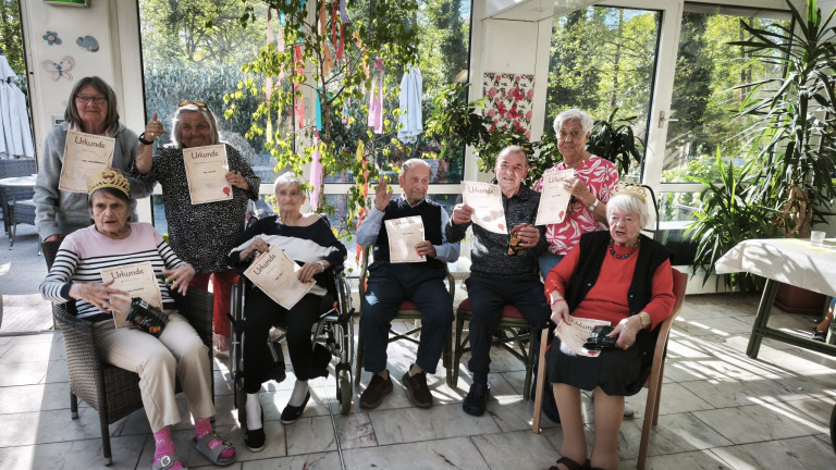 Senioren halten Urkunden in einem sonnigen Gemeinschaftsraum, Gruppenfoto bei einer Ehrung oder Preisverleihung