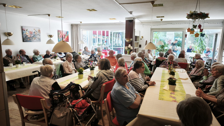 Senioren bei einer Veranstaltung im Gemeinschaftsraum eines Pflegeheims, Frühlingsdekoration auf den Tischen