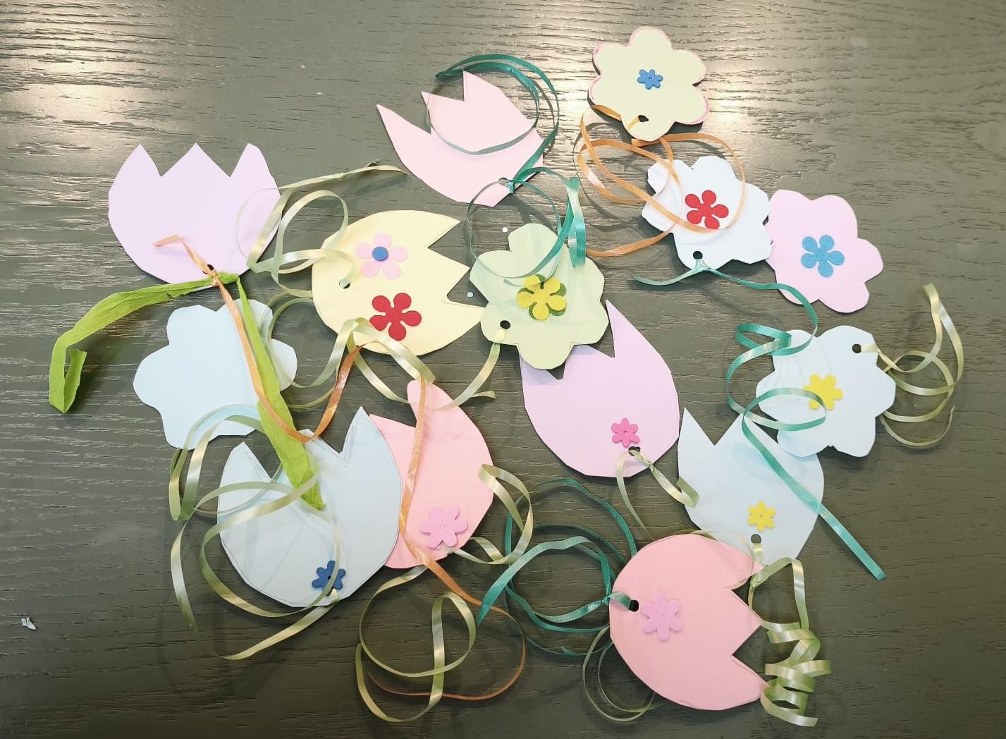 Bunte Papierblumen und Tulpen als Bastel-Deko mit Bändern auf einem Tisch