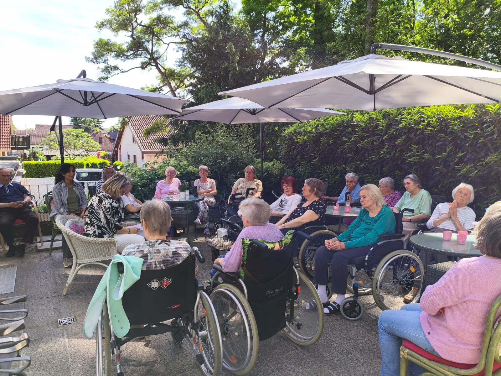 Seniorenrunde im Pflegeheim sitzt gemeinsam im Garten unter Sonnenschirmen