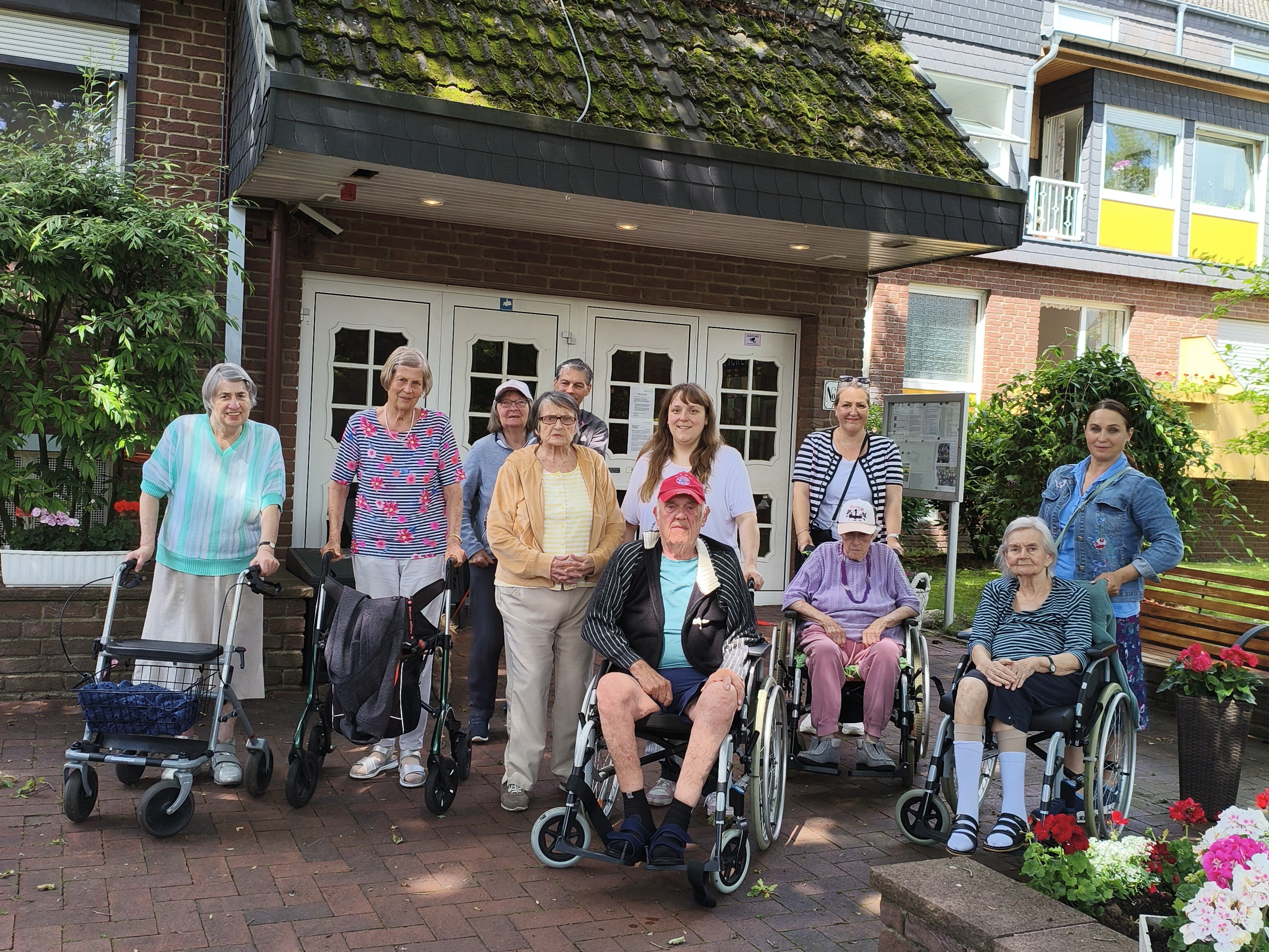 Gruppenfoto von Senioren und Pflegekräften vor einem Altenheim, einige Personen mit Rollatoren und Rollstühlen