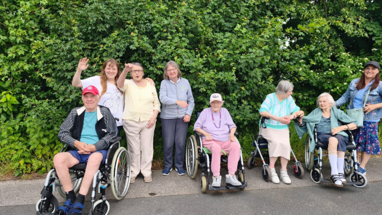 Seniorengruppe mit Rollstuhl und Rollator im Freien vor Hecke Gruppe von Senioren und Seniorinnen im Freien, einige mit Rollstuhl und Rollator, vor einer grünen Hecke